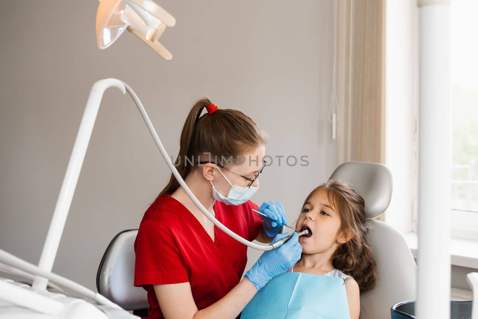 Child dentist with dental drill treats child girl in dentistry clinic. Dental filling for child patient. by Rabizo