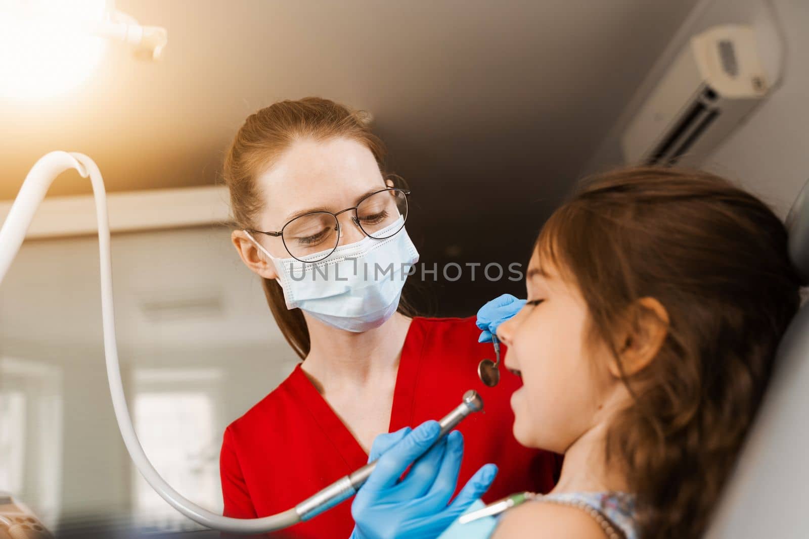 Child dentist with dental drill treats child girl in dentistry clinic. Dental filling for child patient