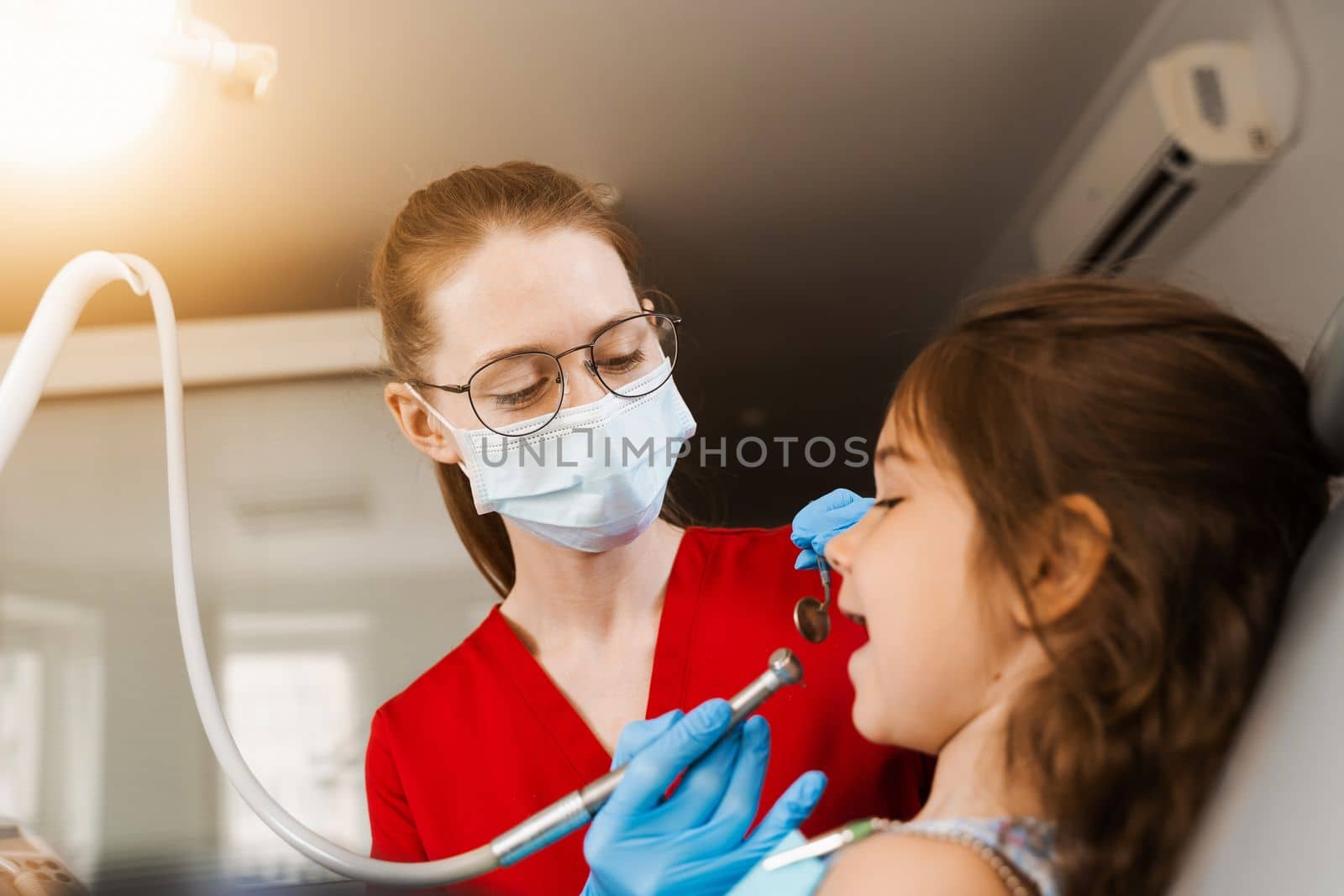 Child dentist with dental drill treats child girl in dentistry clinic. Dental filling for child patient
