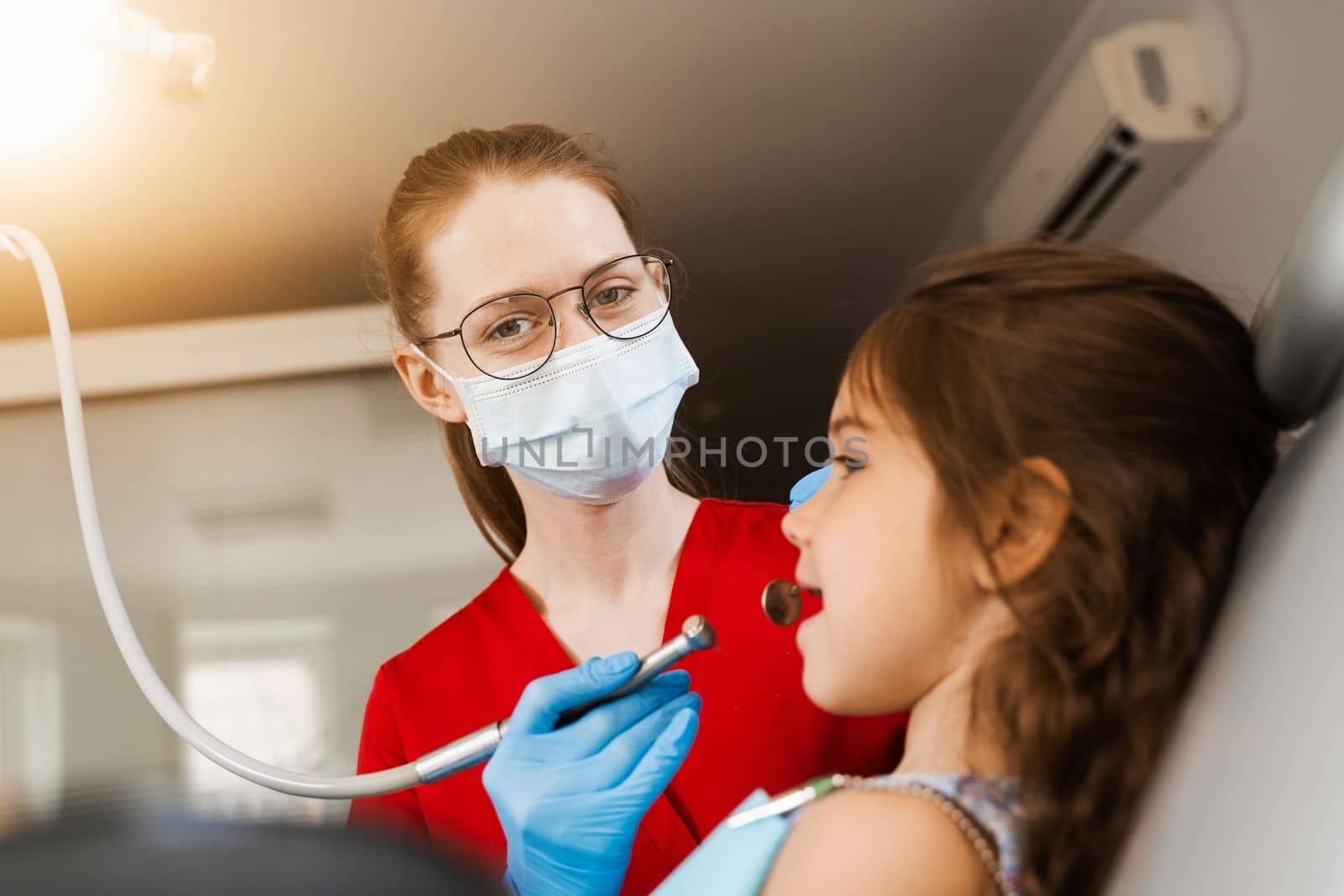 Child dentist with dental drill treats child girl in dentistry clinic. Dental filling for child patient