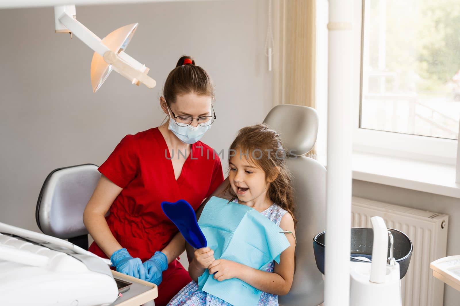 Consultation with child dentist at dentistry. Teeth treatment. Child looking in the mirror at the dentist. Happy child patient of dentistry. by Rabizo