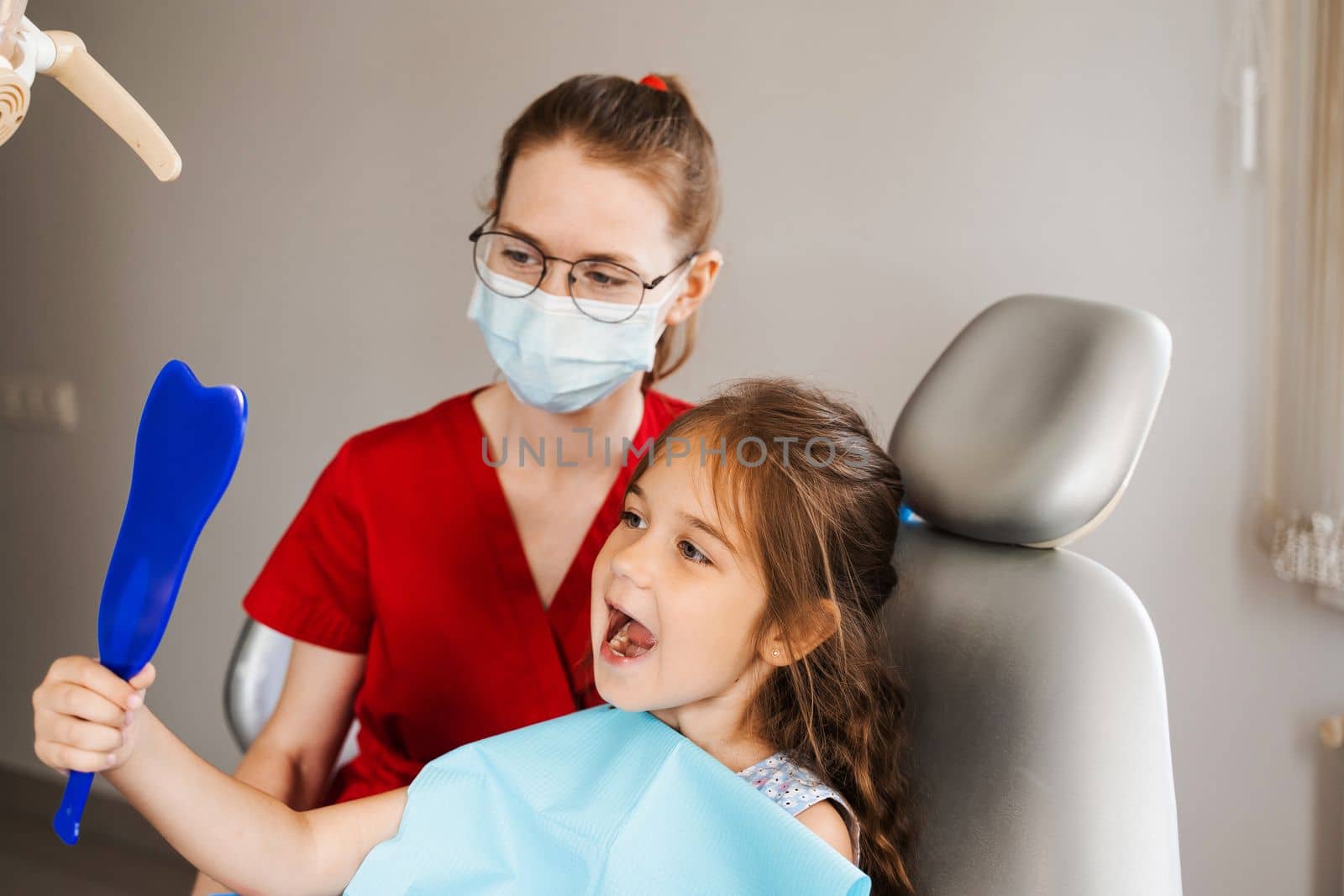 Consultation with child dentist at dentistry. Teeth treatment. Child looking in the mirror at the dentist. Happy child patient of dentistry. by Rabizo