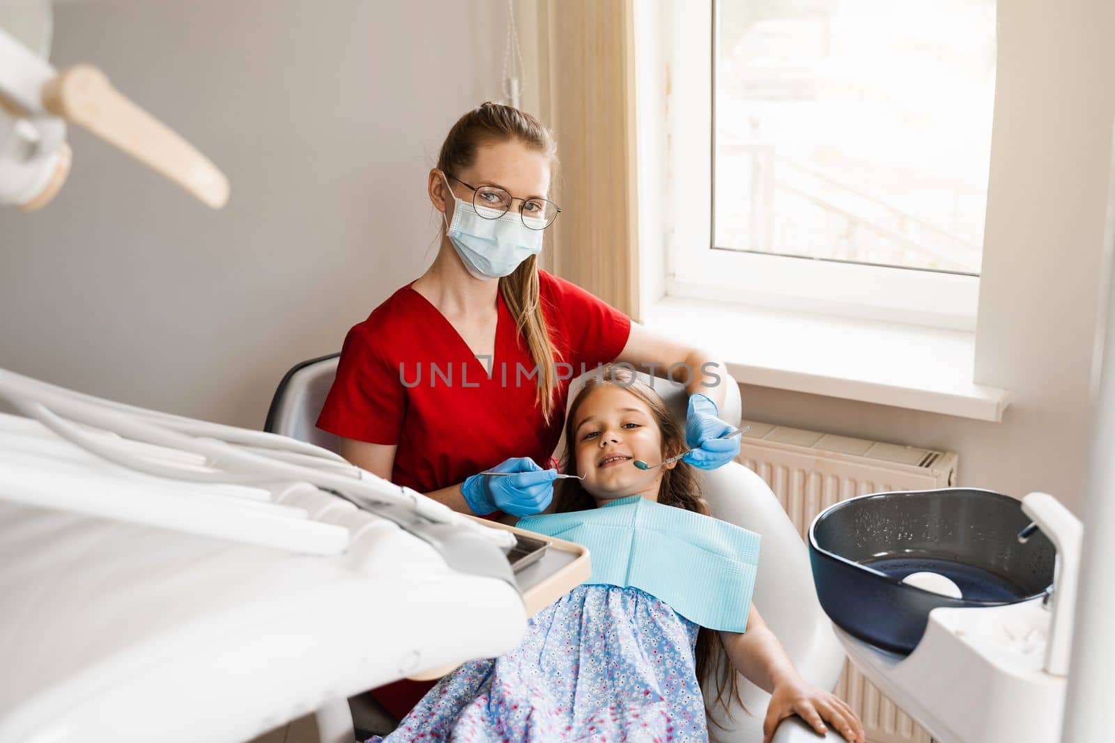 Pediatric dentist and cheerful girl child smiling in dentistry. Child smiles at the consultation with dentist. Creative advertising for dentistry. by Rabizo