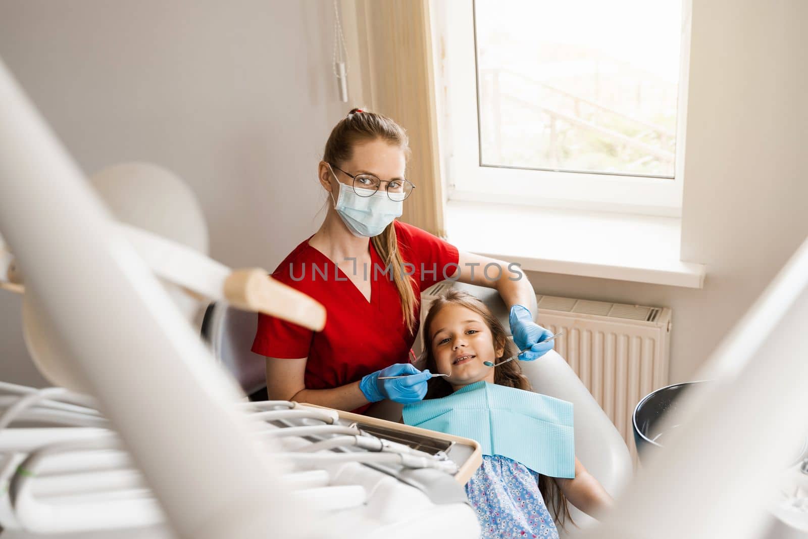 Pediatric dentist and cheerful girl child smiling in dentistry. Child smiles at the consultation with dentist. Creative advertising for dentistry. by Rabizo