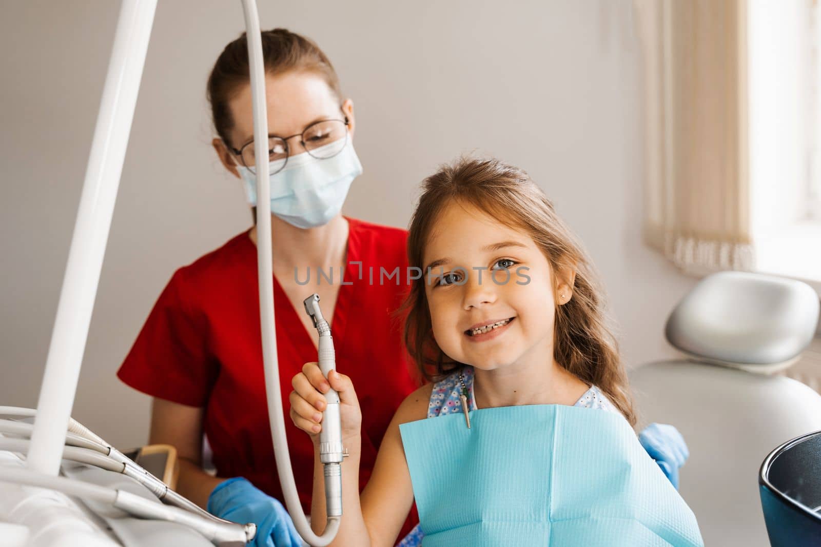 Cheerful girl child holding dental drill and smiling in dentistry. The child smiles at the consultation with the dentist. by Rabizo