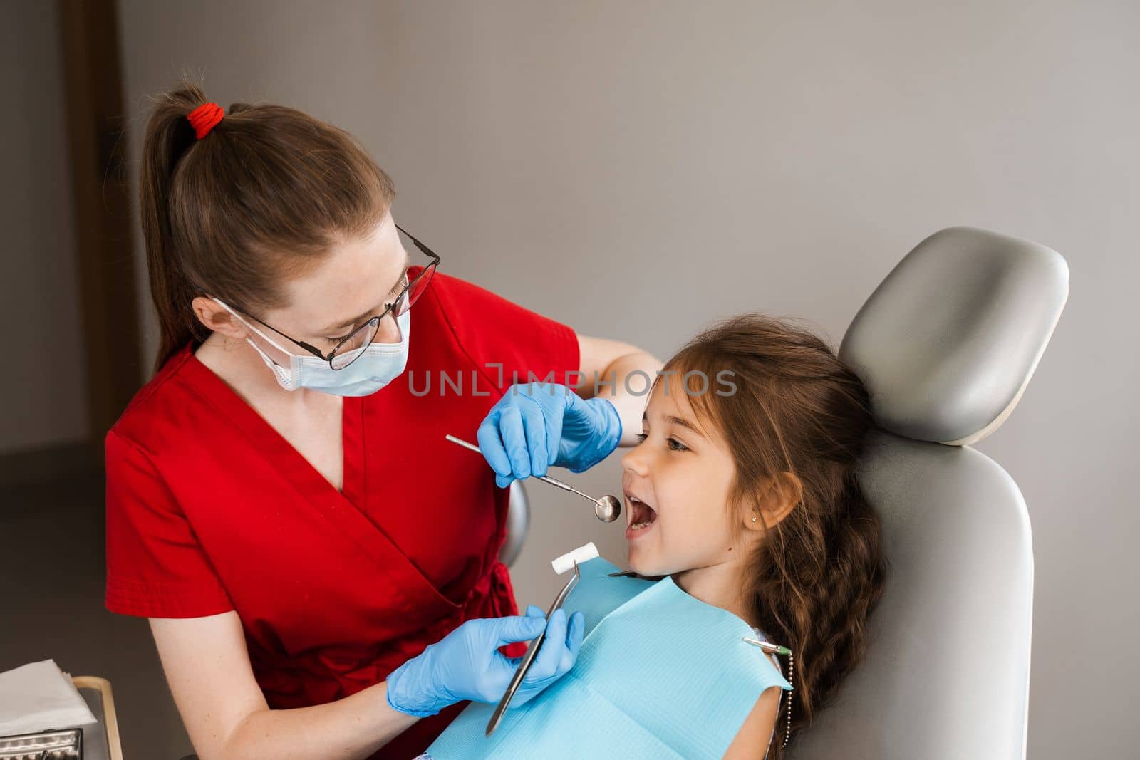 Pediatric dentist puts cotton swab in mouth of a child girl to install a photopolymer dental filling and treat teeth