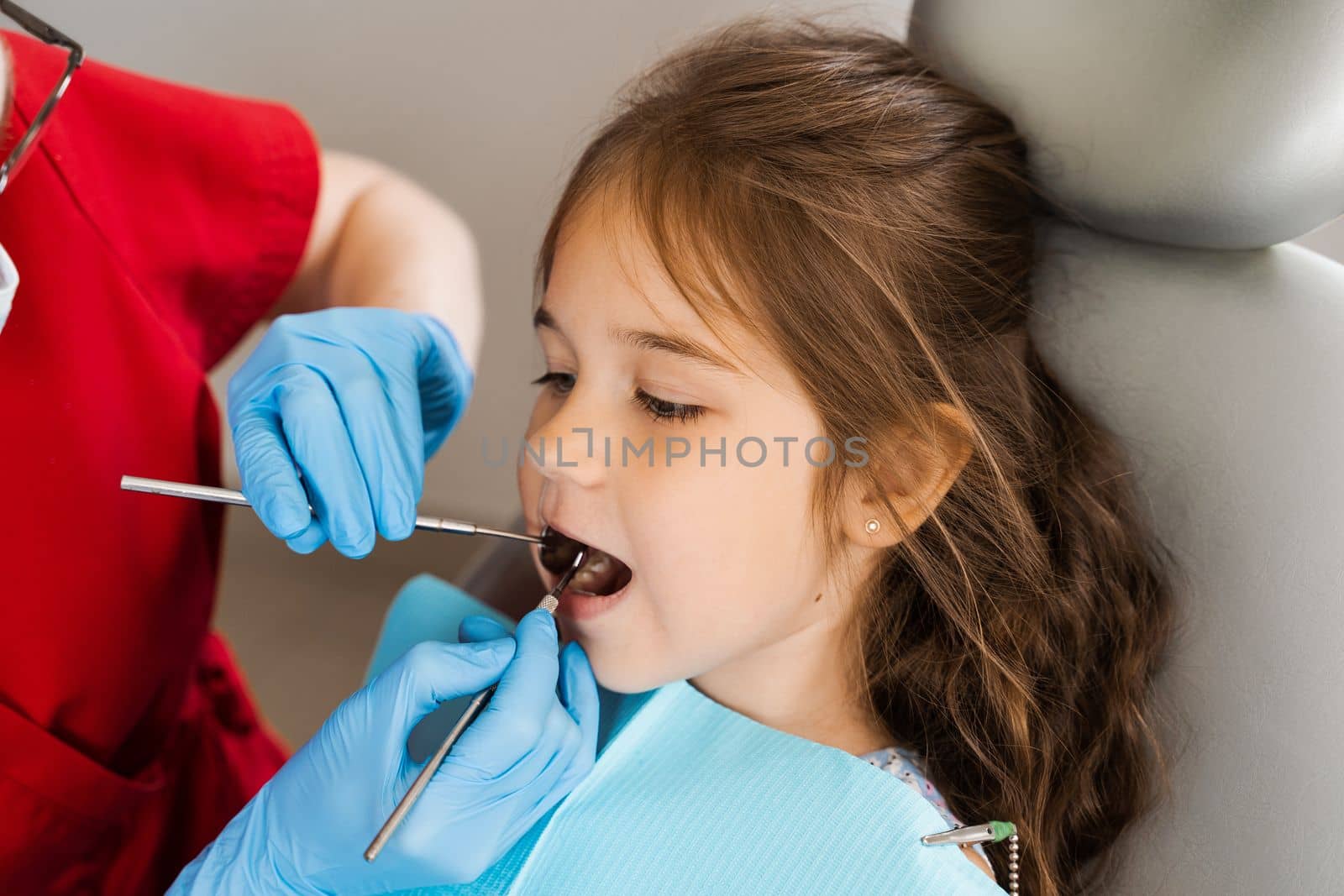 Pediatric dentist examines teeth of child girl for treatment of toothache. Pain in teeth in children. Consultation with pediatric dentist in dentistry. by Rabizo