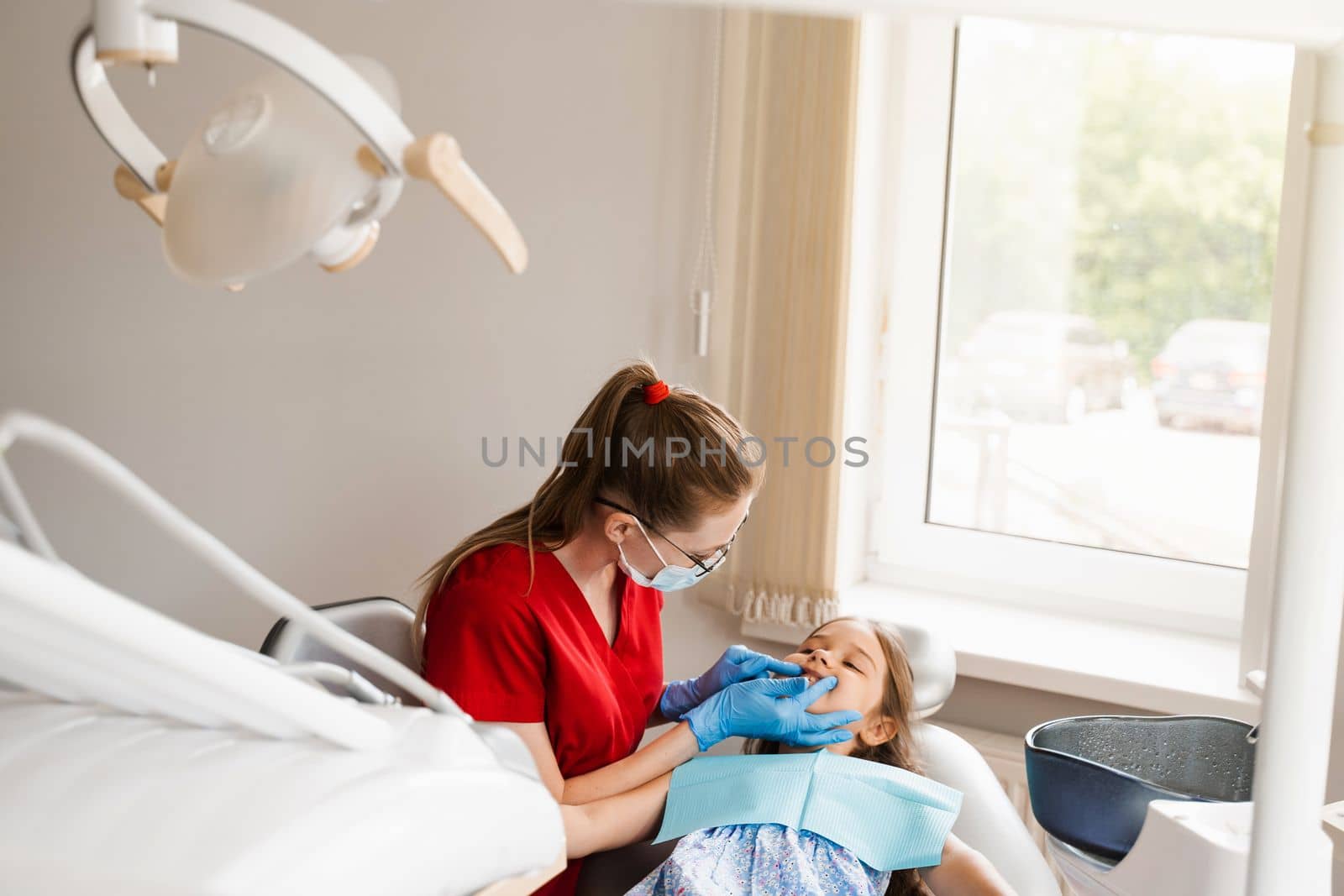 Consultation with child dentist at dentistry. Teeth treatment. Children dentist examines girl mouth and teeth and treats toothaches. Happy child patient of dentistry