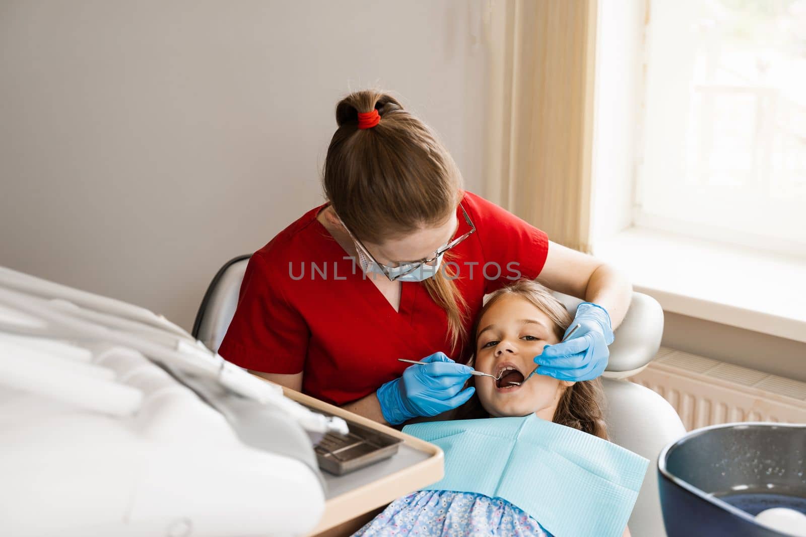 Pediatric dentist and cheerful girl child smiling in dentistry. Child smiles at the consultation with dentist. Creative advertising for dentistry. by Rabizo