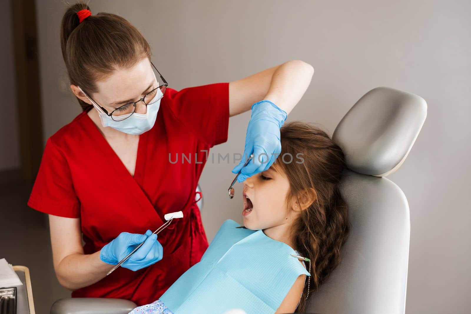 Pediatric dentist puts cotton swab in mouth of a child girl to install a photopolymer dental filling and treat teeth. by Rabizo