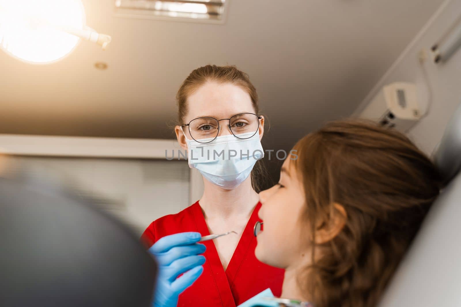 Pediatric dentist examines child girl mouth and teeth and treats toothaches. Happy child patient of dentistry. Consultation with child dentist at dentistry. Teeth treatment. by Rabizo