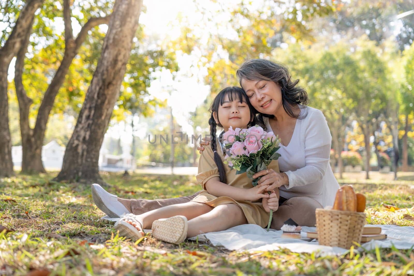 Happy Asian grandmother hugging with her lovely granddaughter in park together. leisure and family concept by nateemee