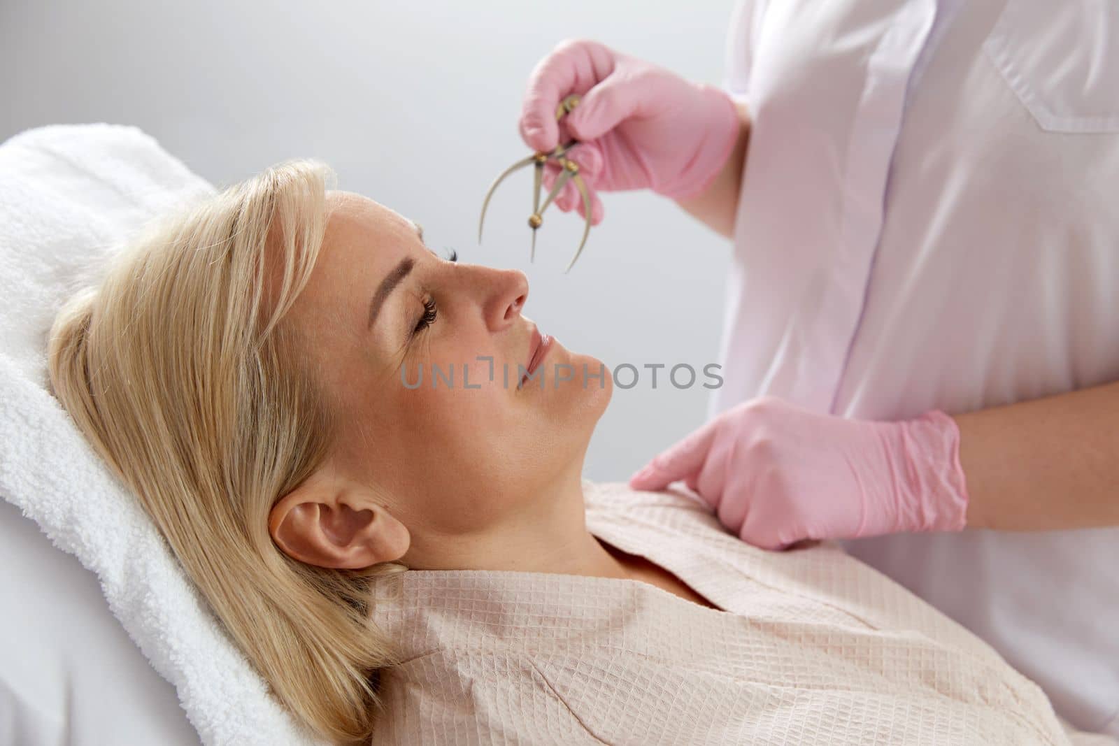 Woman getting her eyebrows angled by a beautician in a beauty salon with instrument by Mariakray