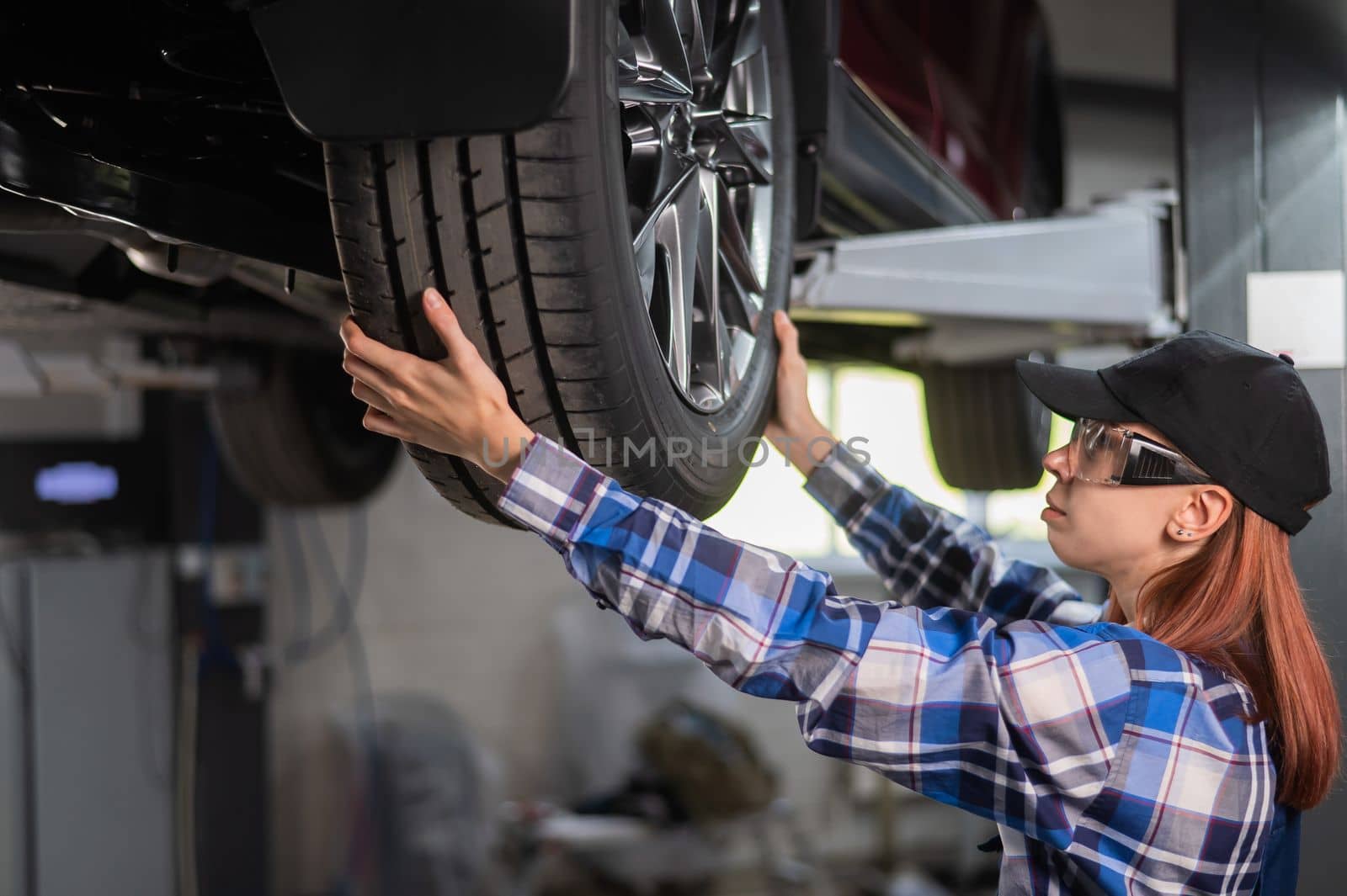 Female mechanic adjusting the tire of the car that is on the lift. A girl at a man's work