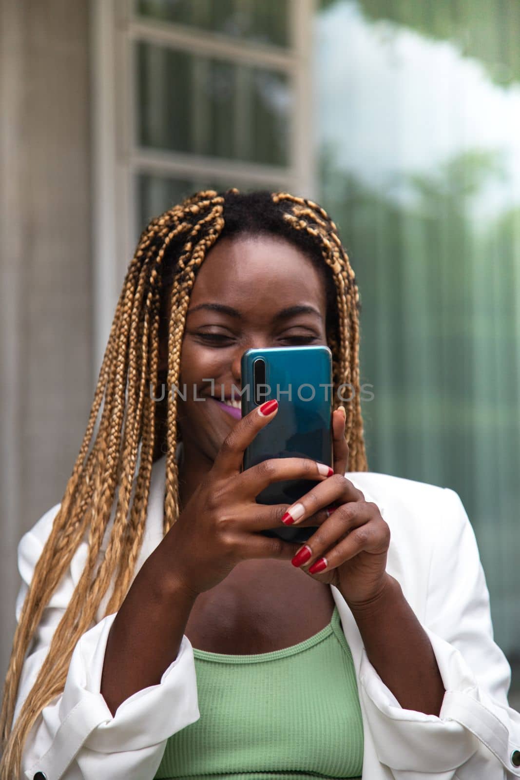 Happy young African American woman with braided hair using mobile phone. Vertical image. by Hoverstock