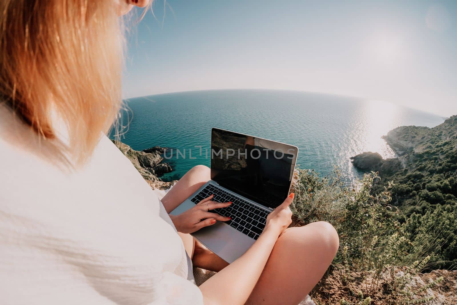 Woman sea laptop. Business woman in yellow hat working on laptop by sea. Close up on hands of pretty lady typing on computer outdoors summer day. Freelance, digital nomad, travel and holidays concept.