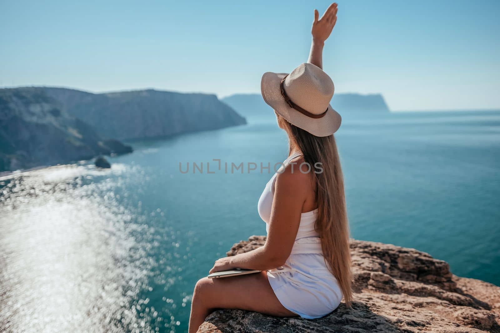 Successful business woman in yellow hat working on laptop by the sea. Pretty lady typing on computer at summer day outdoors. Freelance, travel and holidays concept.