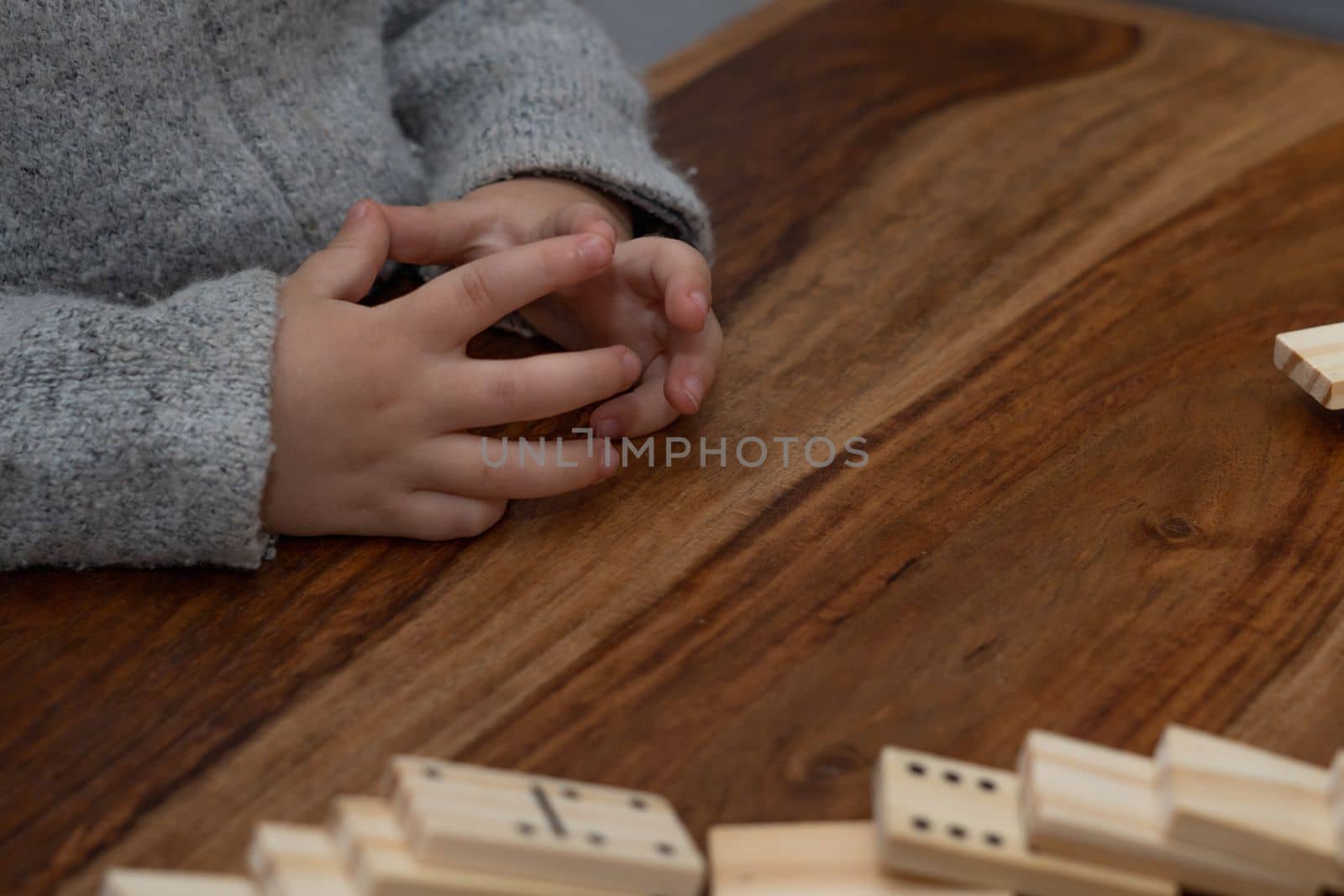 child's hands in gray sweater playing dominoes with blurred focus