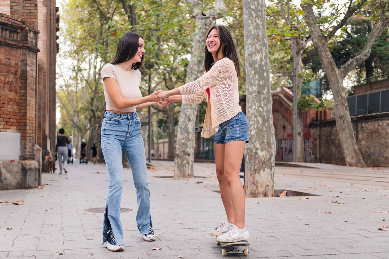 young woman having fun teaching her friend to ride a skateboard, concept of friendship and teenager lifestyle