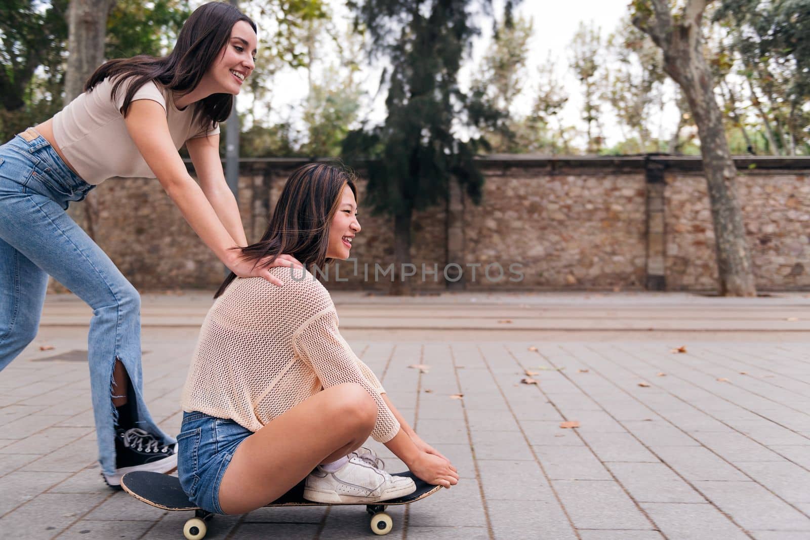 young couple of friends laughing and having fun playing with a skateboard down a city street, concept of friendship and teenager lifestyle, copy space for text