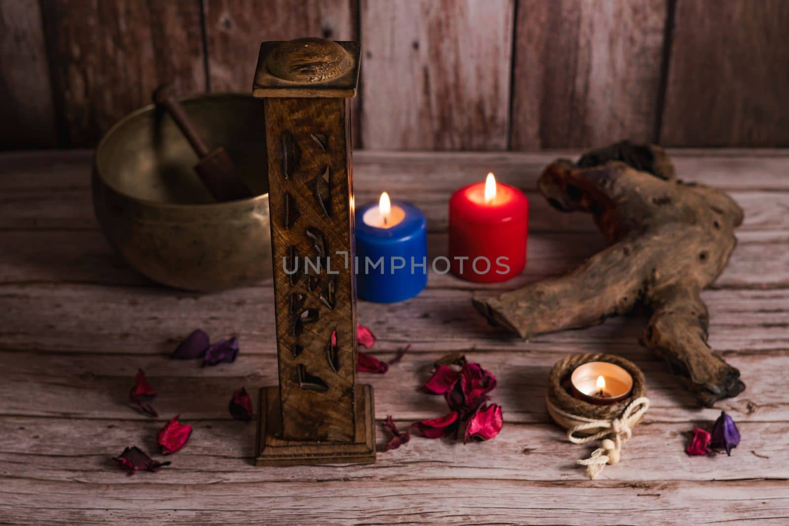 carved wooden incense burner with lighted colored candles and Tibetan bowl in the background