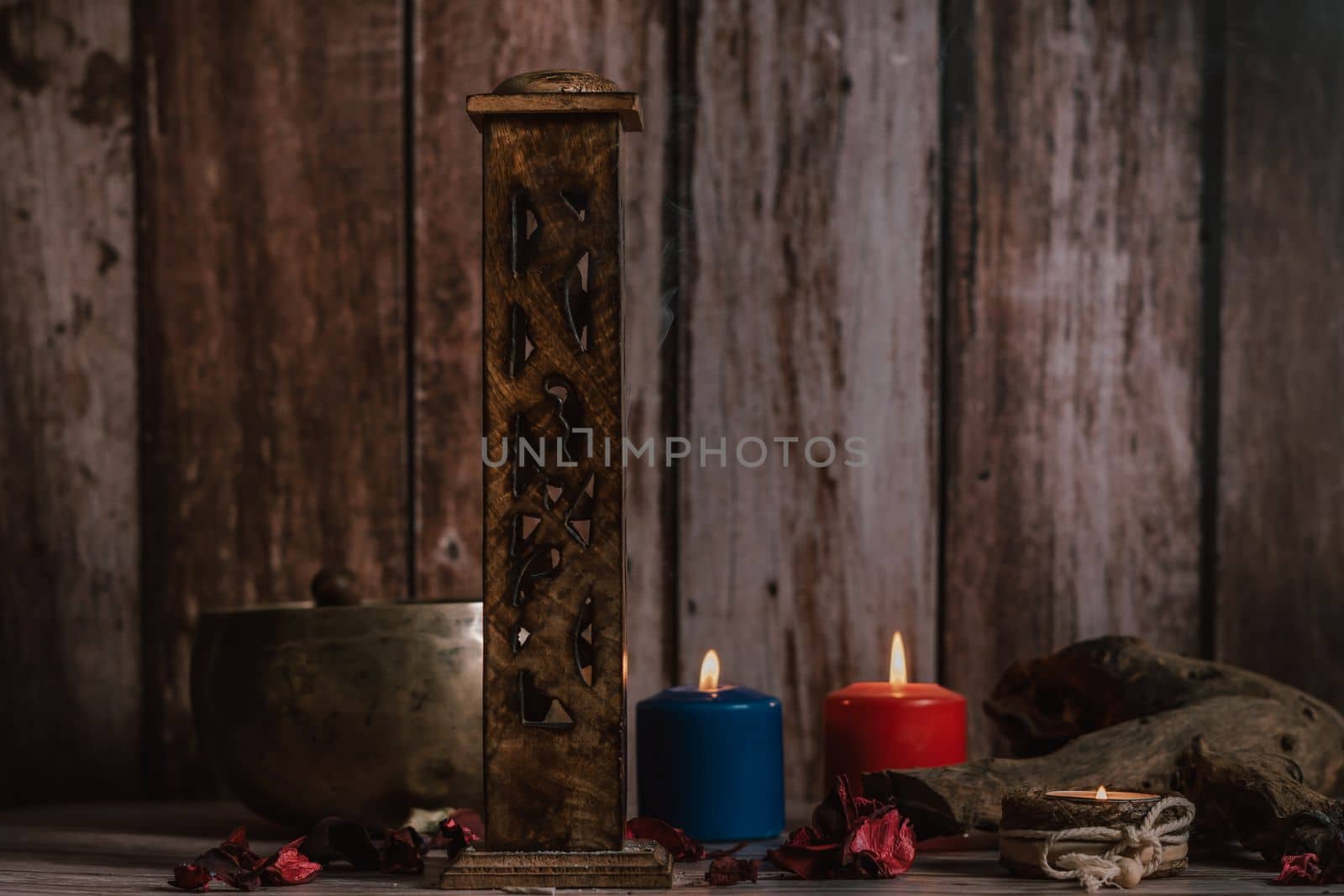 carved wooden incense burner with lighted colored candles and Tibetan bowl in the background