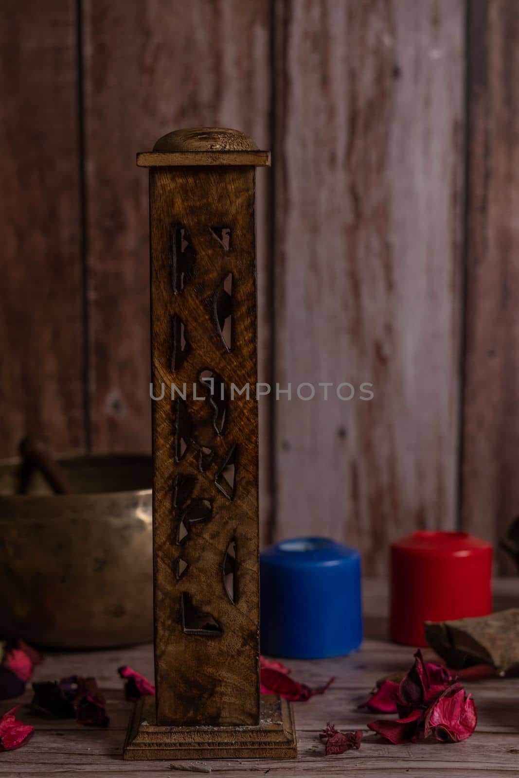carved wooden incense burner with lighted colored candles and Tibetan bowl in the background