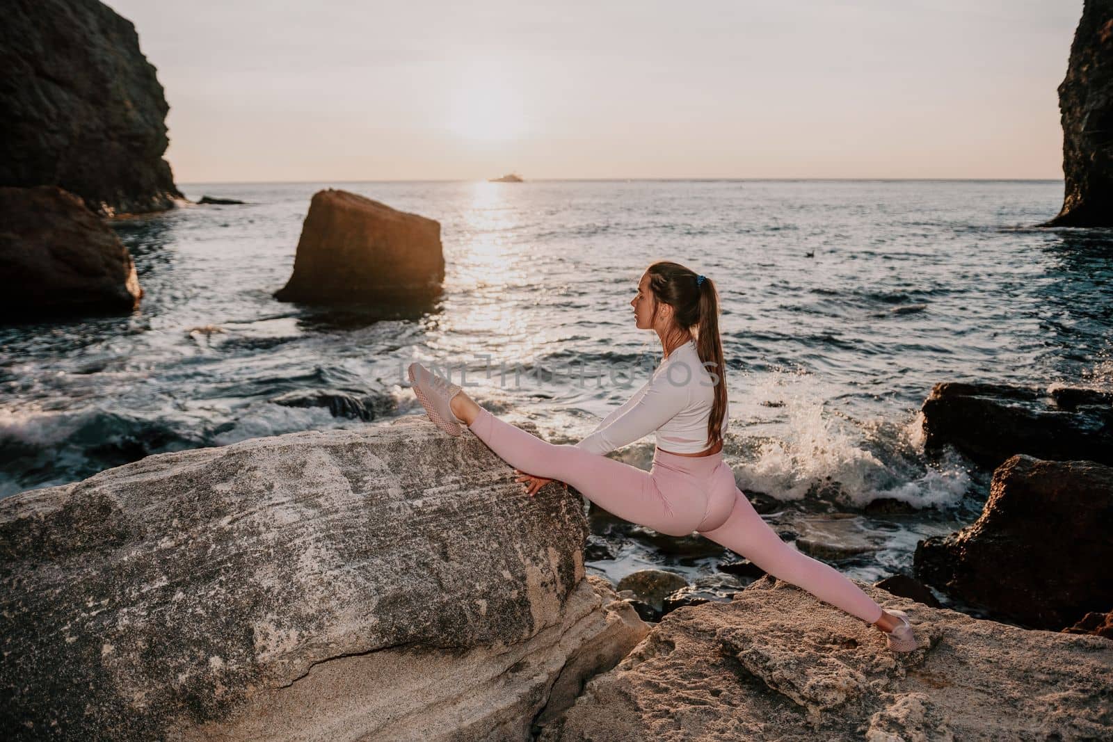 Young woman with black hair, fitness instructor in pink sports leggings and tops, doing pilates on yoga mat with magic pilates ring by the sea on the beach. Female fitness daily yoga concept