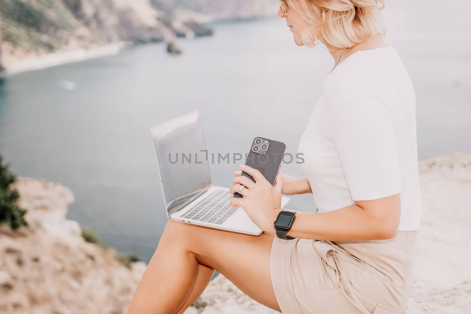 Digital nomad, Business woman working on laptop by the sea. Pretty lady typing on computer by the sea at sunset, makes a business transaction online from a distance. Freelance remote work on vacation