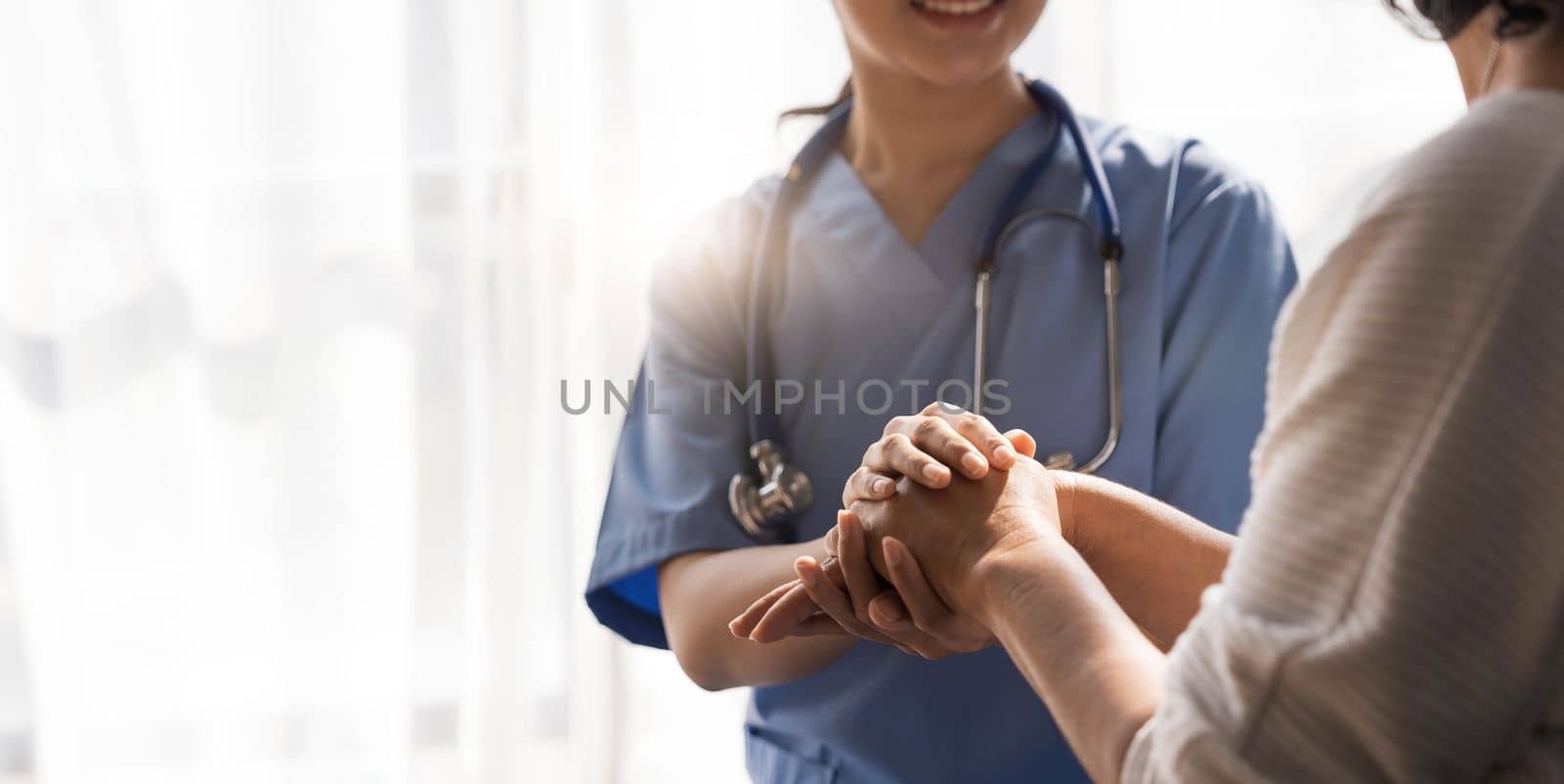 Closeup Happy patient is holding caregiver for a hand while spending time together. Elderly woman in nursing home and nurse...