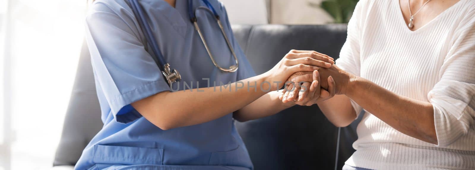 Closeup Happy patient is holding caregiver for a hand while spending time together. Elderly woman in nursing home and nurse...