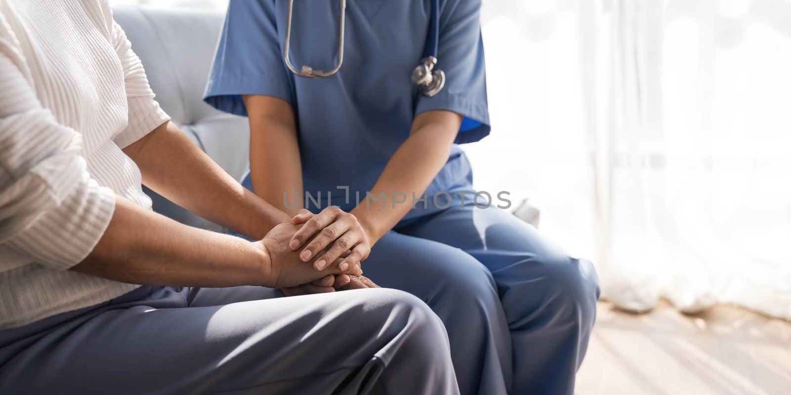 Closeup Happy patient is holding caregiver for a hand while spending time together. Elderly woman in nursing home and nurse...