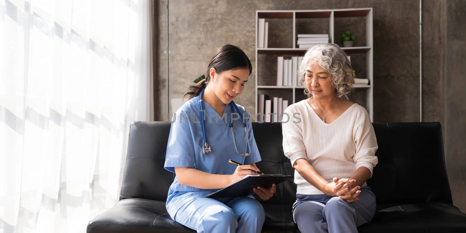 Happy patient is holding caregiver for a hand while spending time together. Elderly woman in nursing home and nurse...