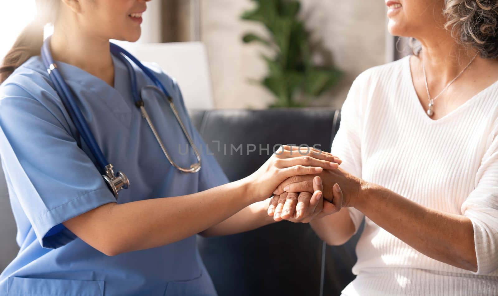 Closeup Happy patient is holding caregiver for a hand while spending time together. Elderly woman in nursing home and nurse. by wichayada