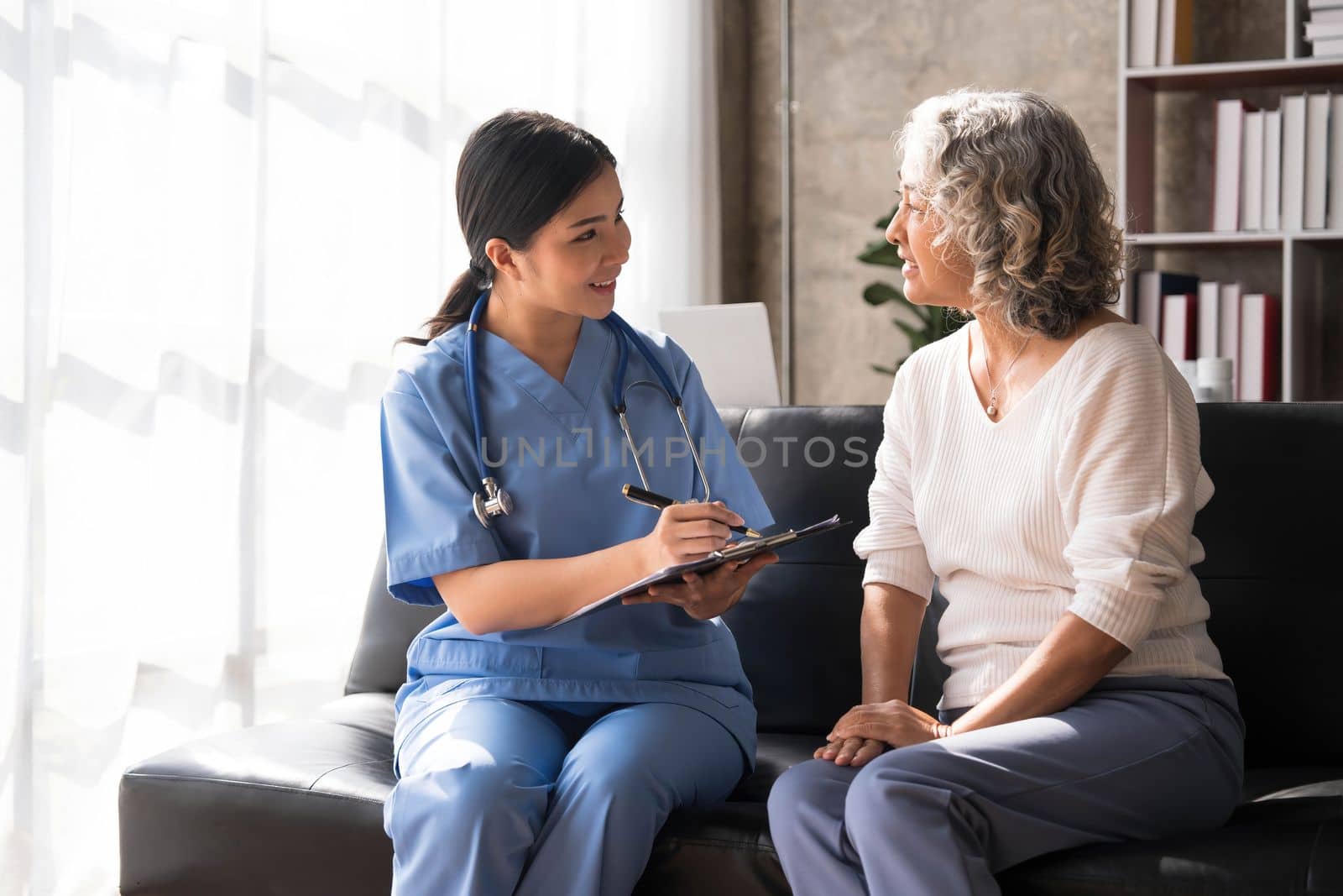 Happy patient is holding caregiver for a hand while spending time together. Elderly woman in nursing home and nurse...