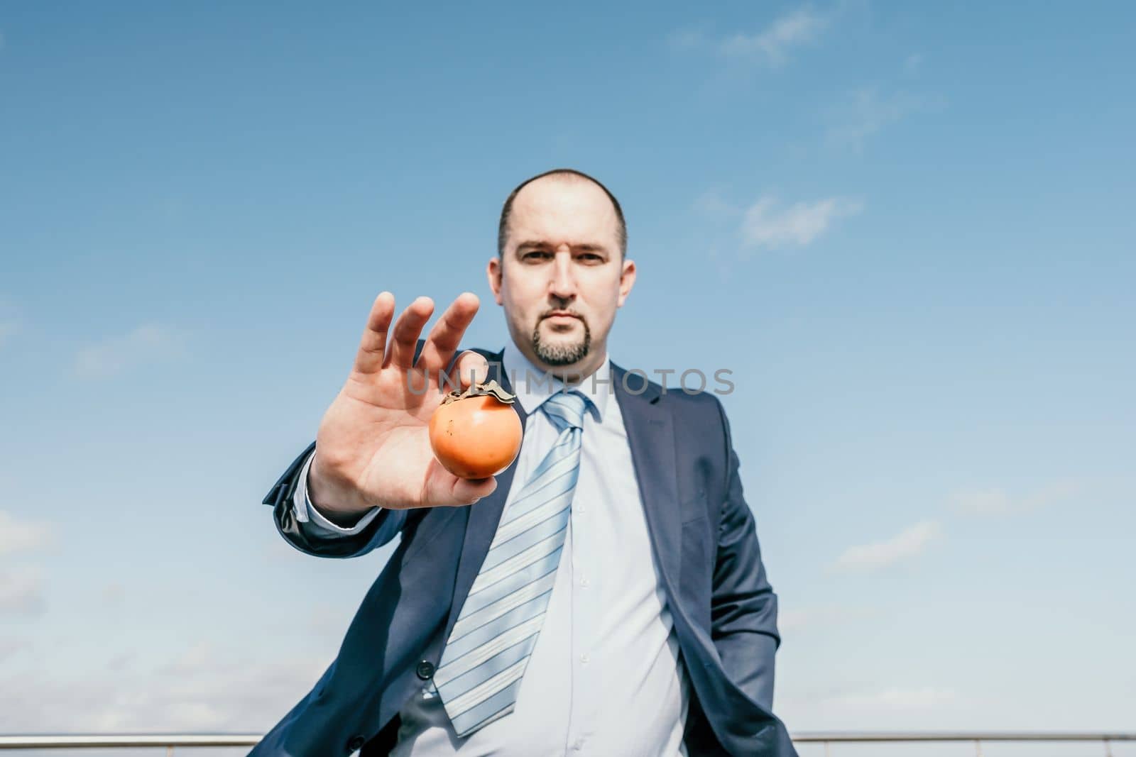 Male persimmon park. Hipster millennial man in a tie and jacket bites off a persimmon while sitting on a park bench in slow motion Young business people eat golden persimmons at lunchtime