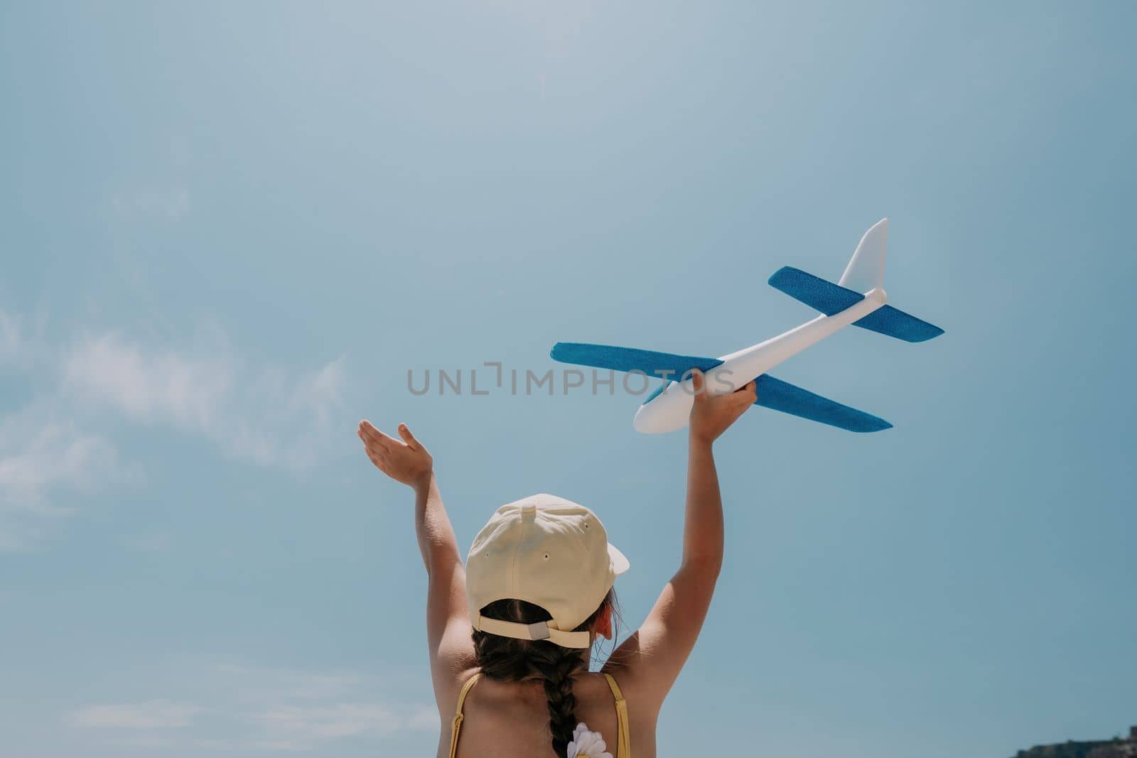 Kid playing with toy airplane. Children dream of travel by plane. Happy child girl has fun in summer vacation by sea and mountains. Outdoors activities at background of blue sky. Lifestyle moment. by panophotograph