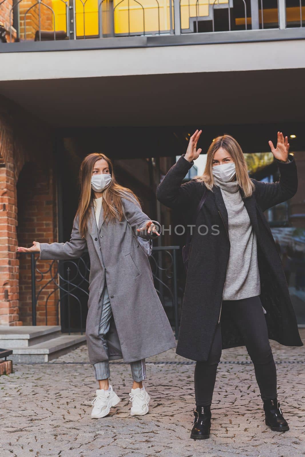 Young pretty girls friends in medical masks having fun and dance outdoor in autumn evening in city laughing and going crazy - end of pandemic concept by Satura86