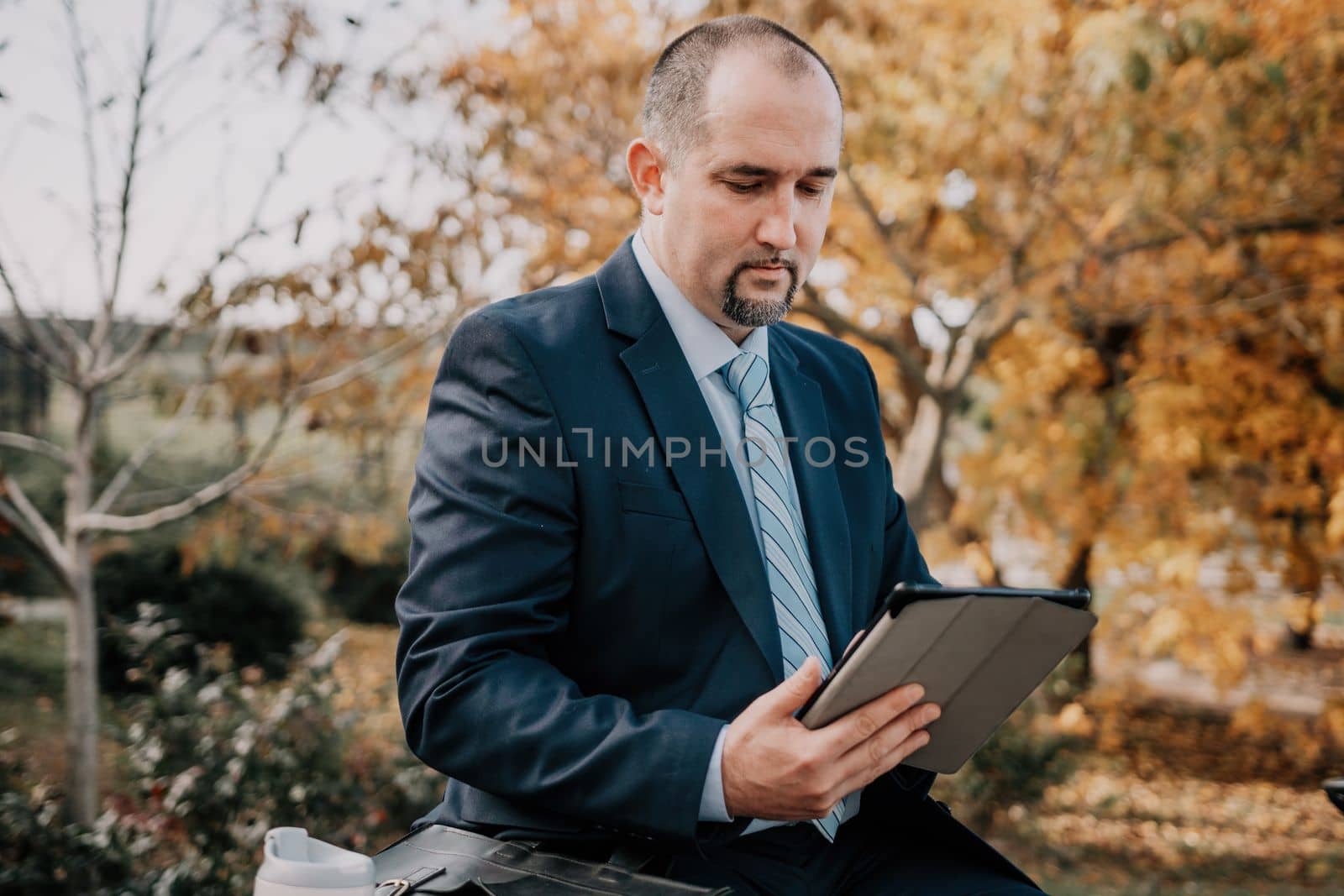 Mature entrepreneur drink coffee in autumn park. Senior executive rest in city park.