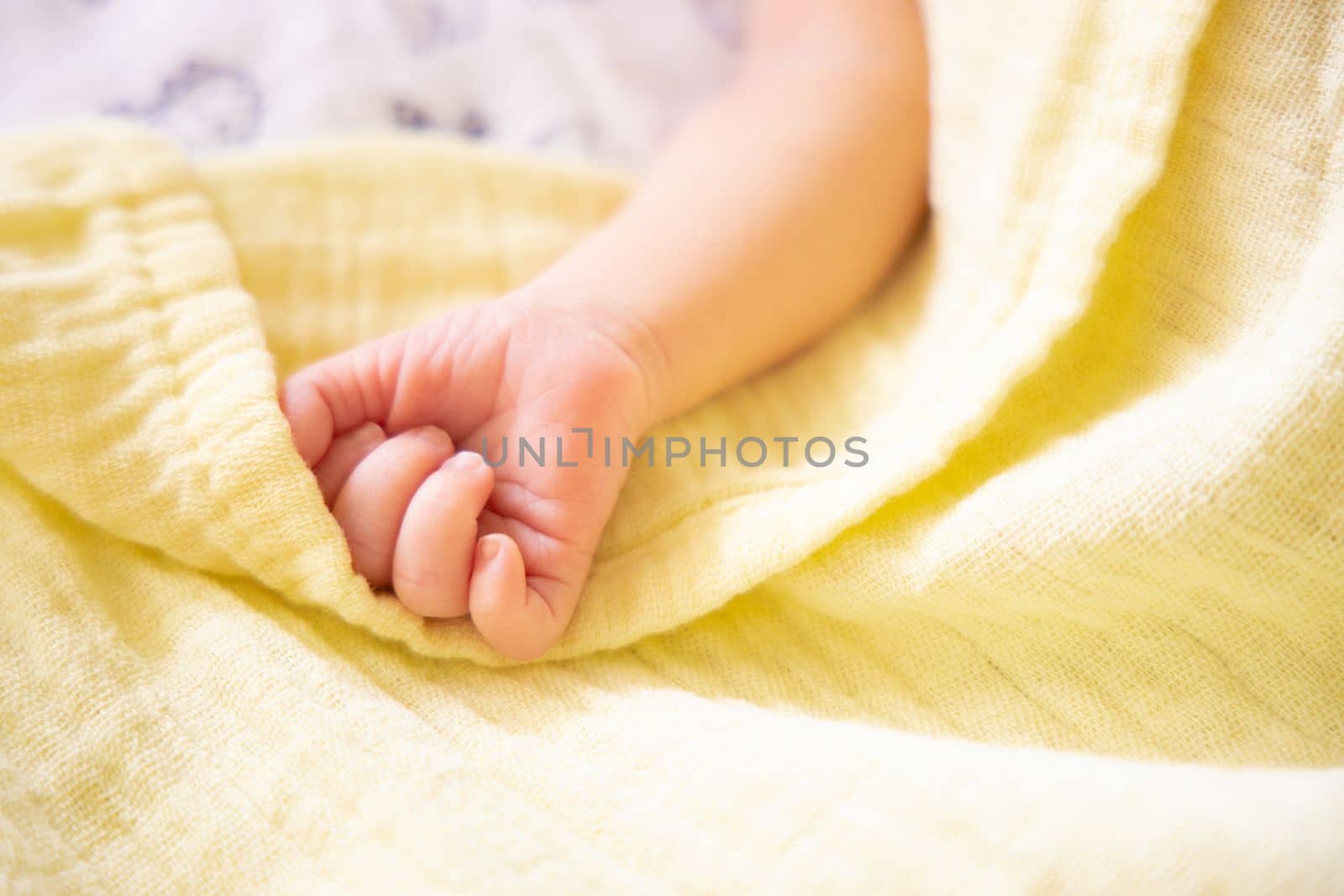 Newborn caucasian premature baby hand on pastel yellow soft muslin blanket soft focus. Copy space, space for text. by Ri6ka