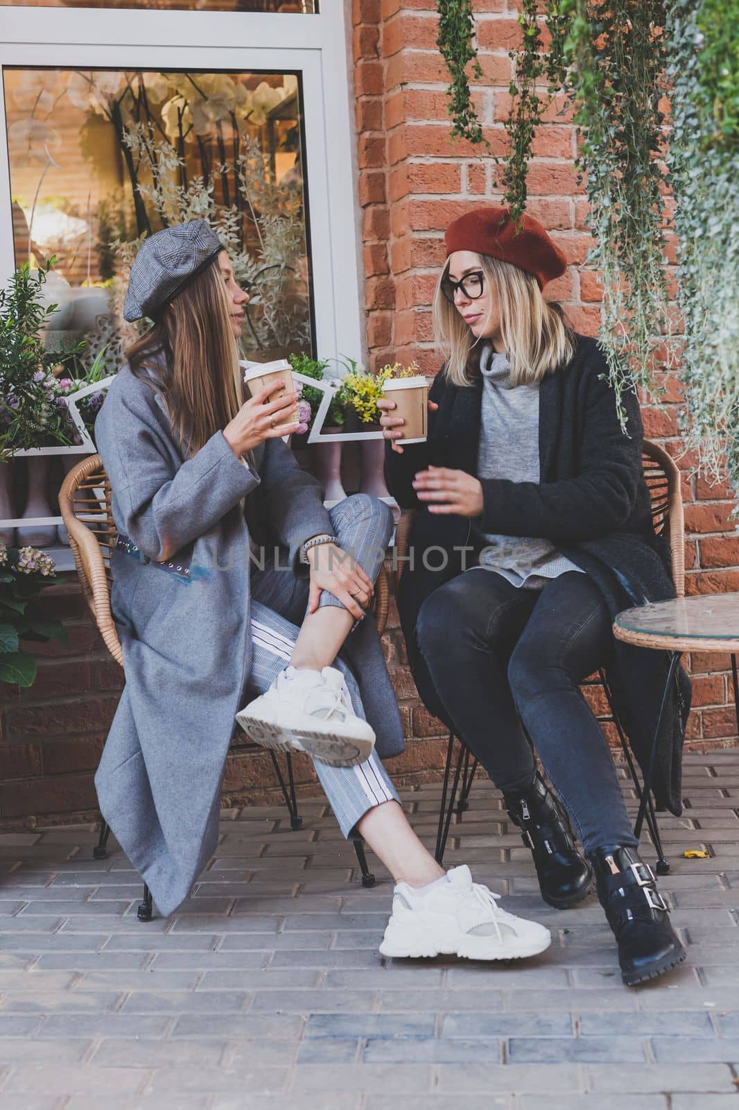 Young female best friends talking to each other discussing interesting themes during free time hipster girls joking and having fun together enjoying recreation with coffee to go on urban background by Satura86