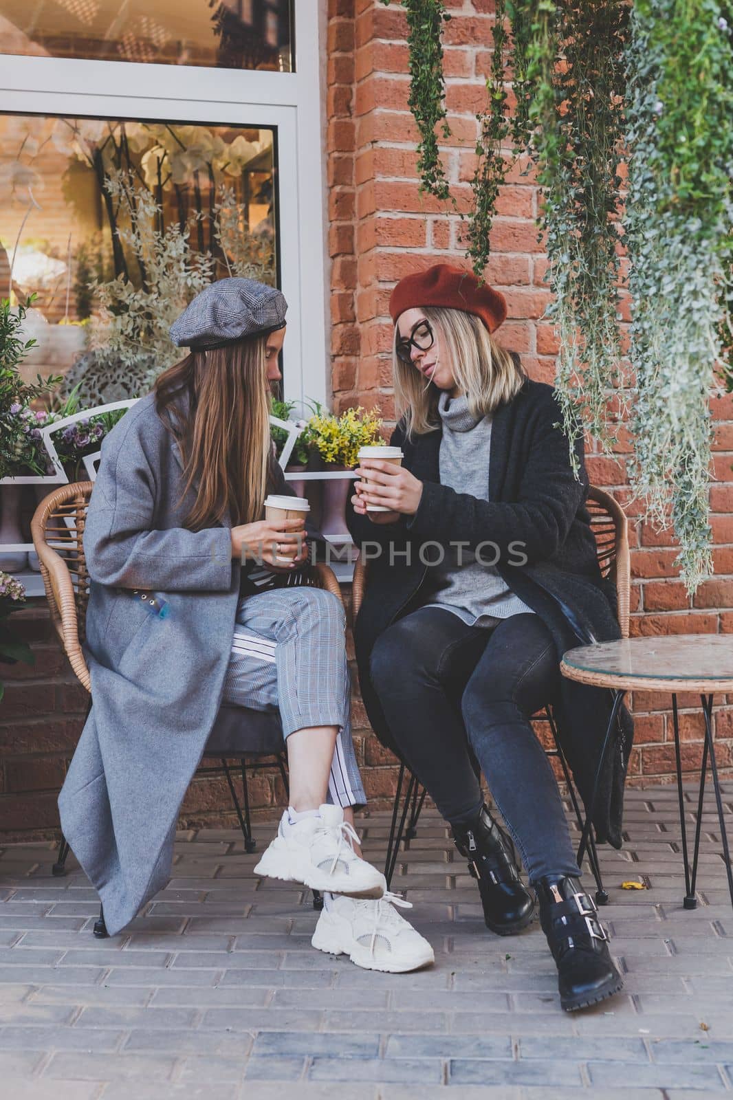Young female best friends talking to each other discussing interesting themes during free time hipster girls, joking and having fun together enjoying recreation with coffee to go on urban