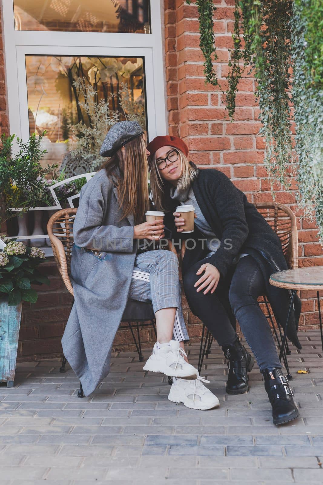 Young female best friends talking to each other discussing interesting themes during free time hipster girls joking and having fun together enjoying recreation with coffee to go on urban background by Satura86