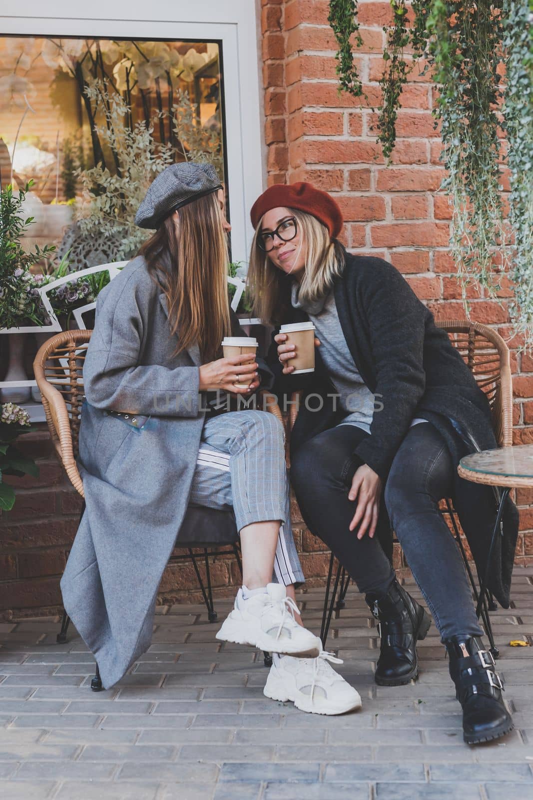 Young female best friends talking to each other discussing interesting themes during free time hipster girls, joking and having fun together enjoying recreation with coffee to go on urban
