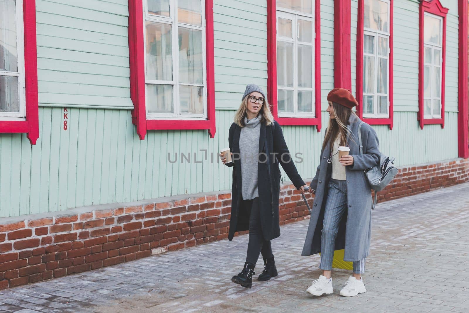 Two cheerful tourist women smiling and walking with suitcases on city street in autumn or spring time - travel and vacation concept by Satura86