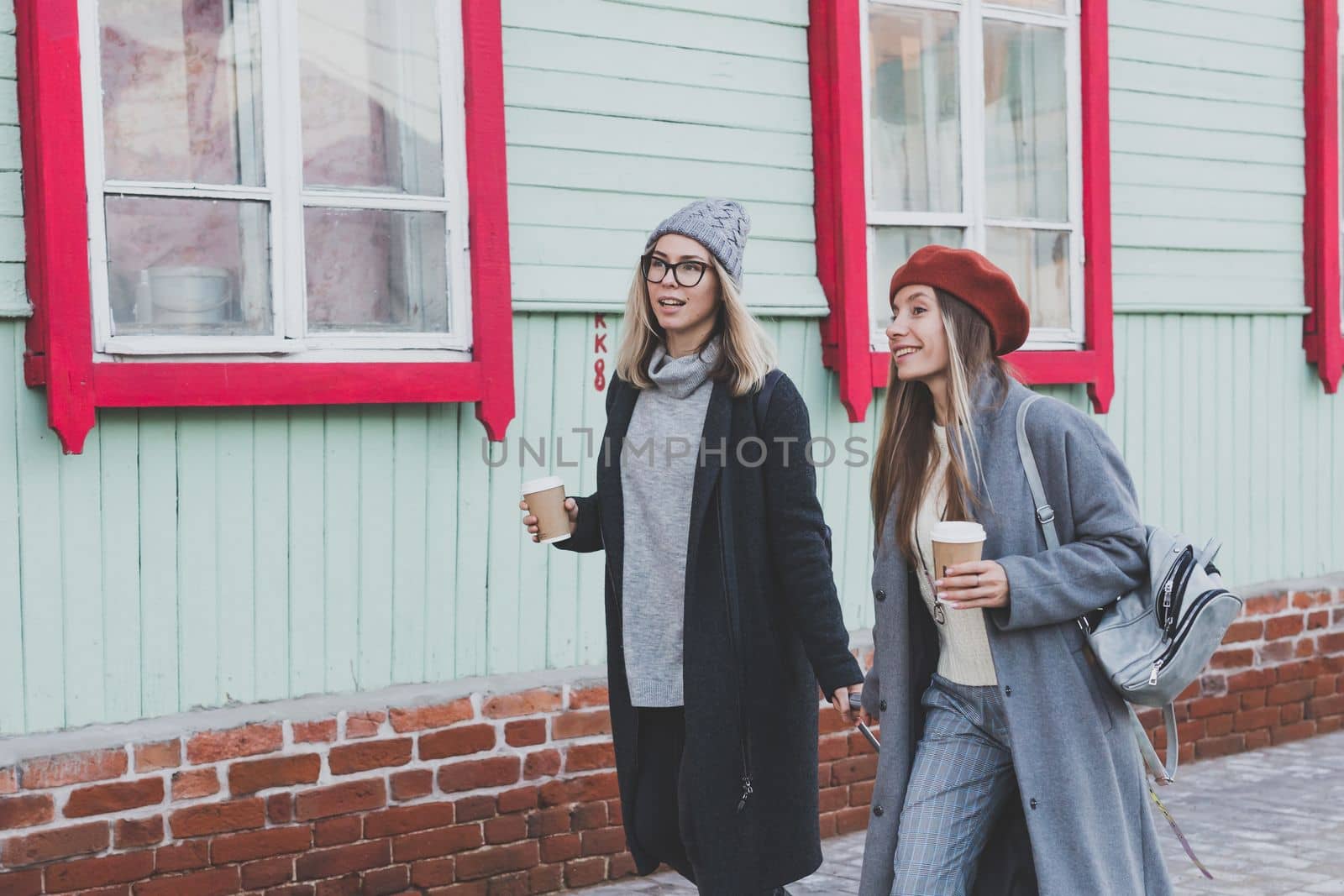 Two cheerful tourist women smiling and walking with suitcases on city street in autumn or spring time - travel and vacation concept by Satura86