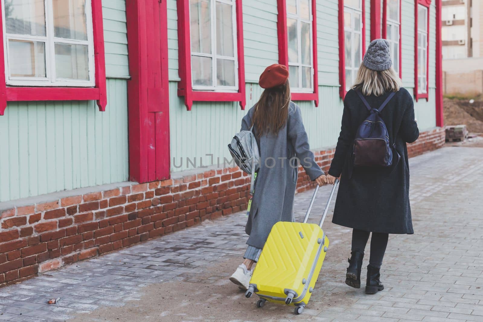 Two cheerful tourist women smiling and walking with suitcases on city street in autumn or spring time - travel and vacation concept by Satura86