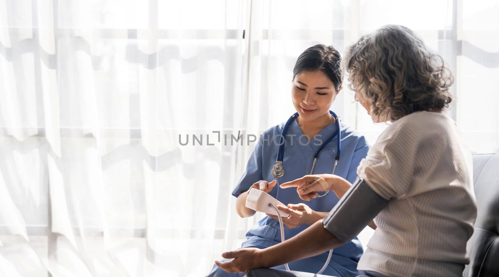 Happy senior woman having her blood pressure measured in a nursing home by her caregiver. Happy nurse measuring blood pressure of a senior woman in living room..