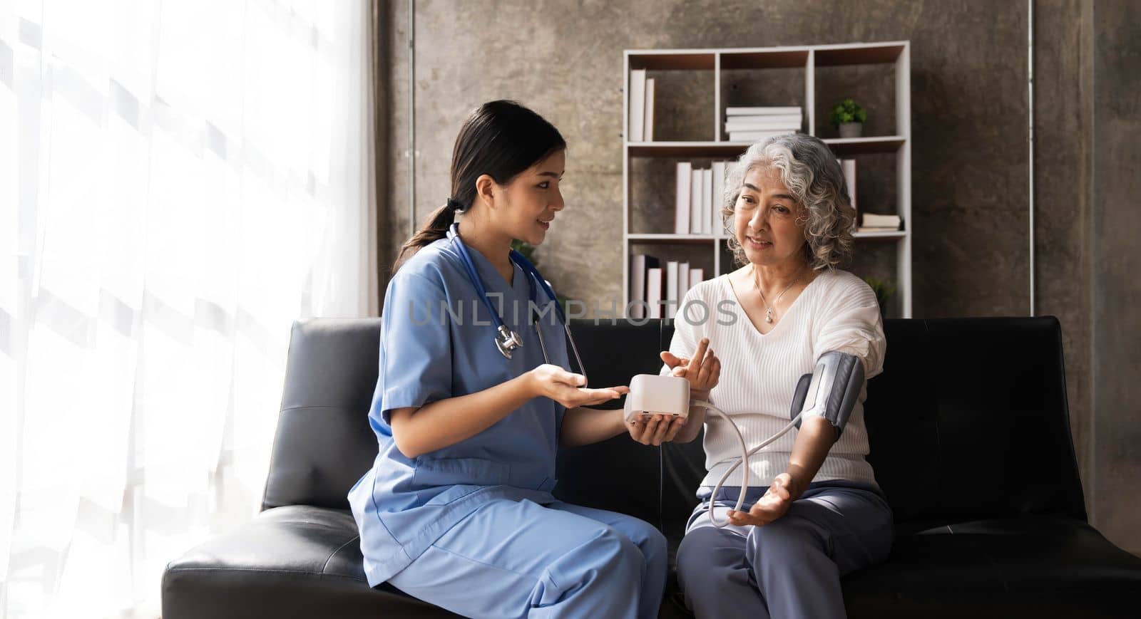 Happy senior woman having her blood pressure measured in a nursing home by her caregiver. Happy nurse measuring blood pressure of a senior woman in living room..