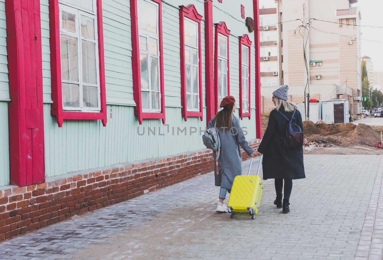 Two cheerful tourist women smiling and walking with suitcases on city street in autumn or spring time - travel and vacation concept by Satura86